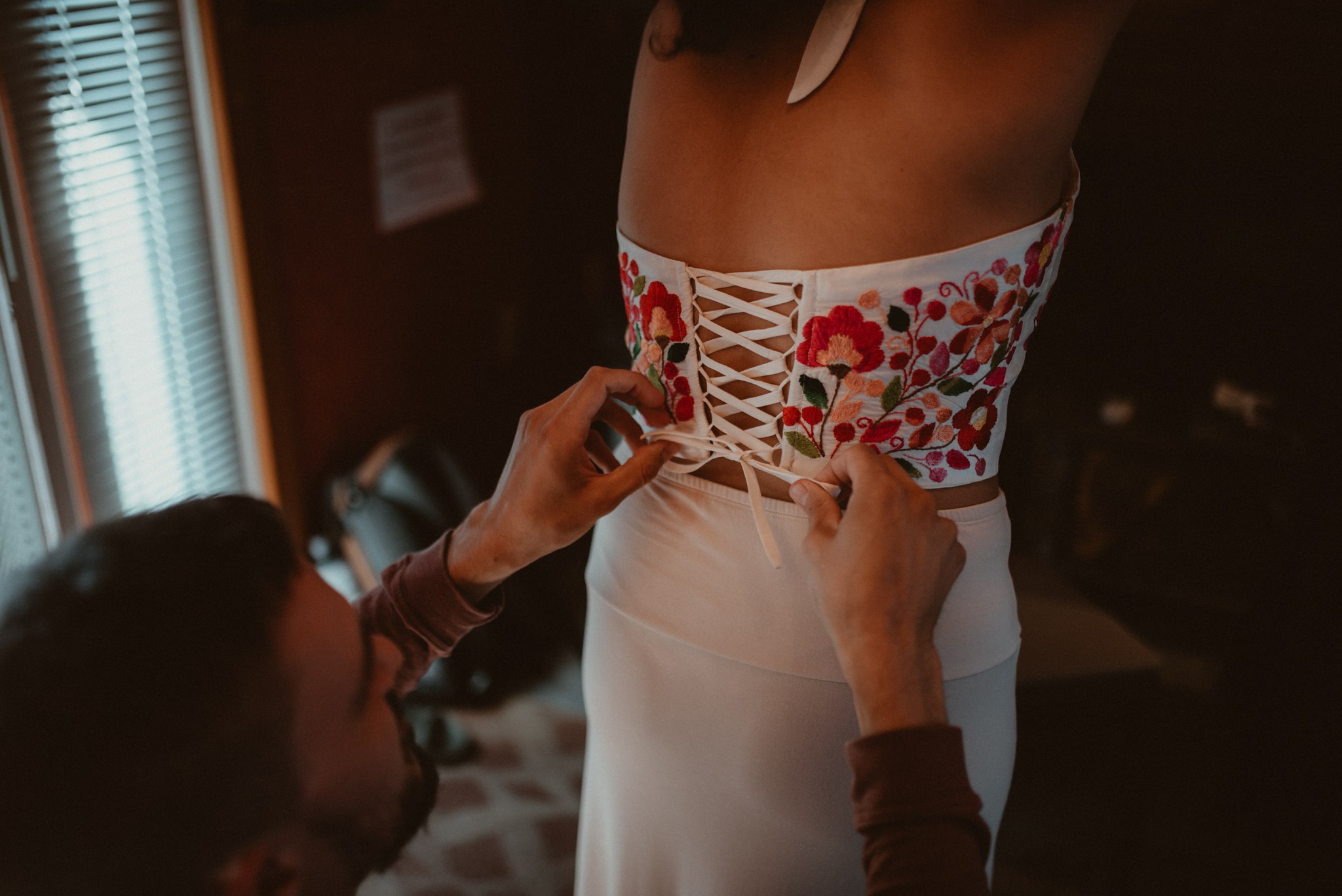 Groom tying the back of a Mexican wedding outfit