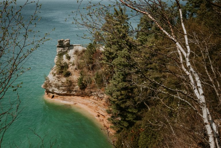 Turquoise water and sandstone cliff shoreline at Pictured Rocks National Lakeshore in Michigan, surrounded by pine trees