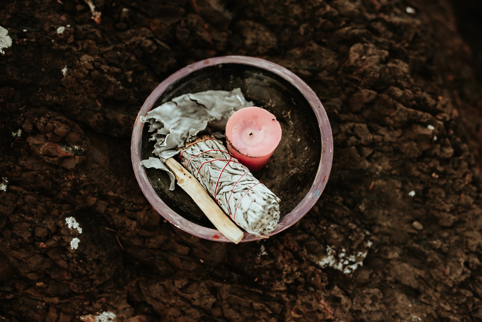 A bowl on the ground containing Reiki ceremony items- sage, a candle, and crystals.