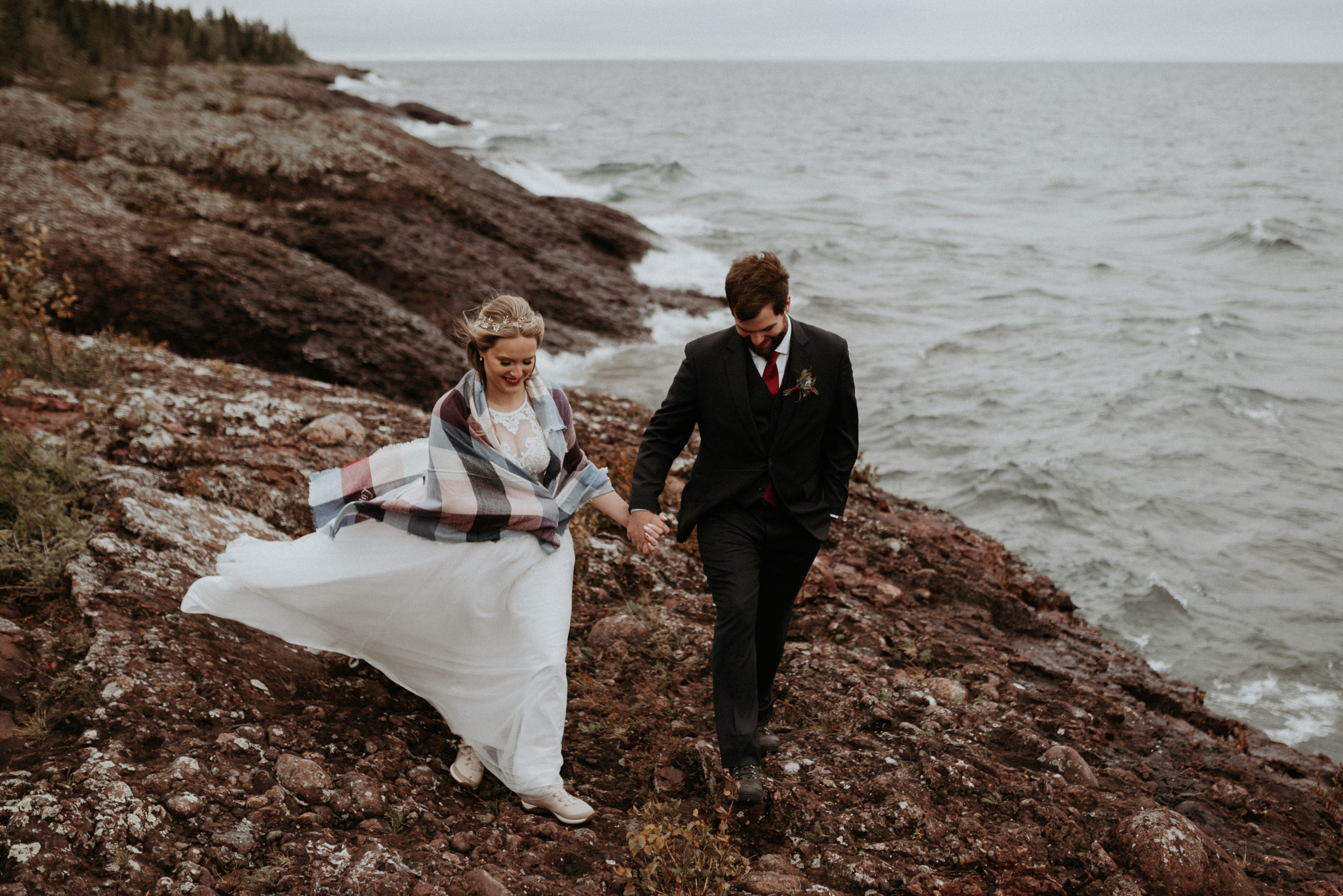 Bride and groom walking hand in hand on the edge of Lake Superior at an elopement in Copper Harbor, Upper Peninsula of Michigan