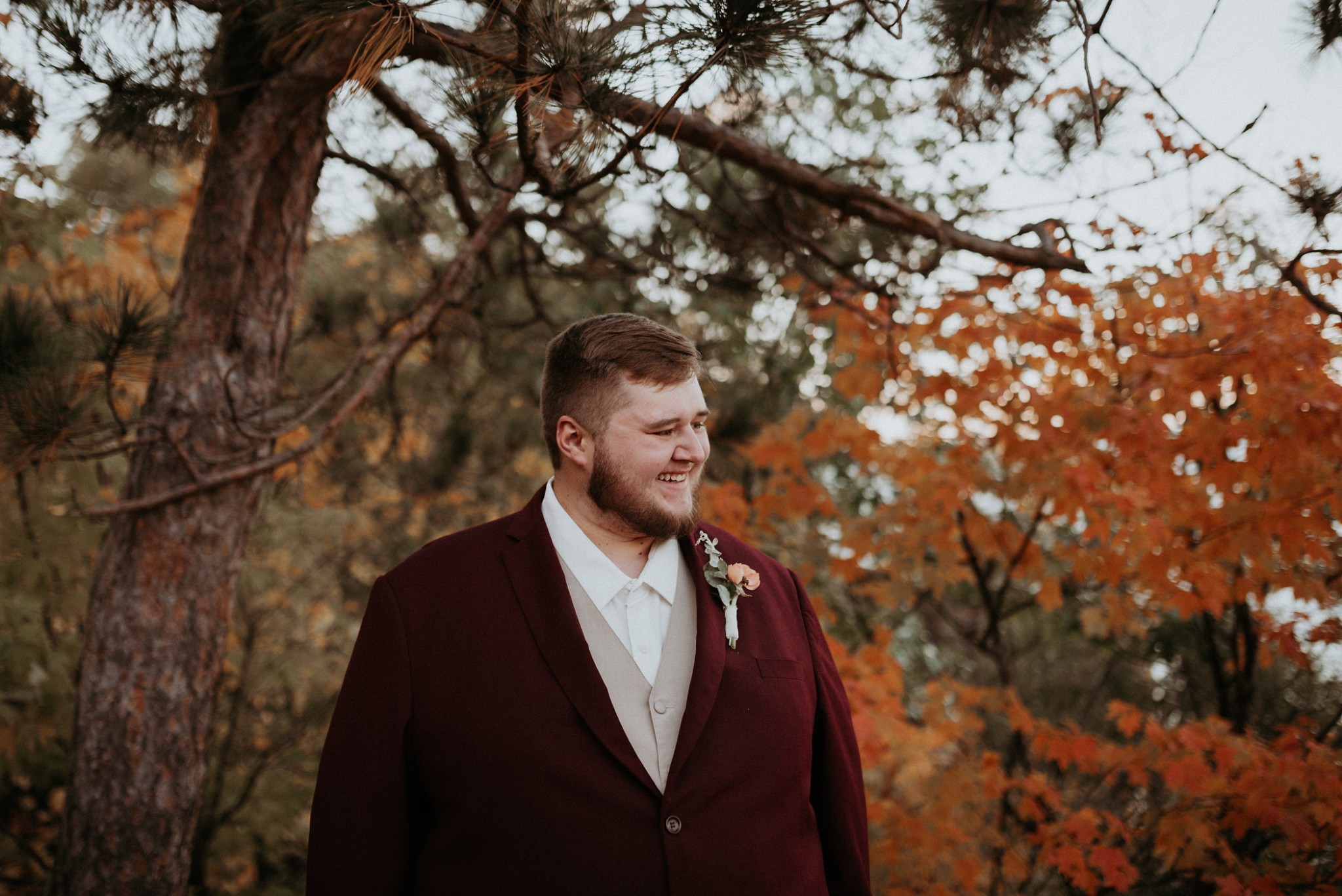 Groom smiling and in a dark red suit.