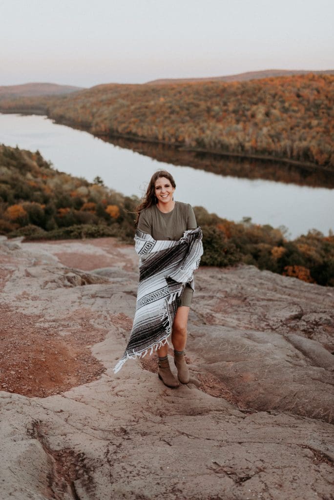 Young adult girl with long brown hair smiling at the Lake of the Clouds in Michigan.