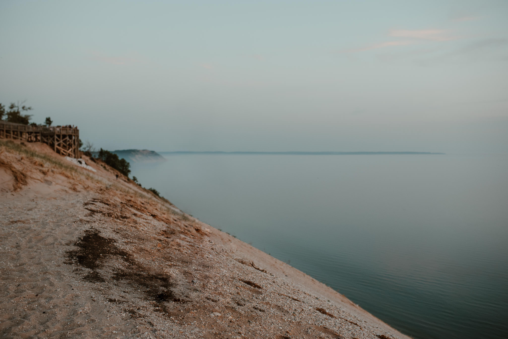 Calm Lake Michigan shoreline with sandy bluffs and soft blue sky, representing elopement locations across Michigan