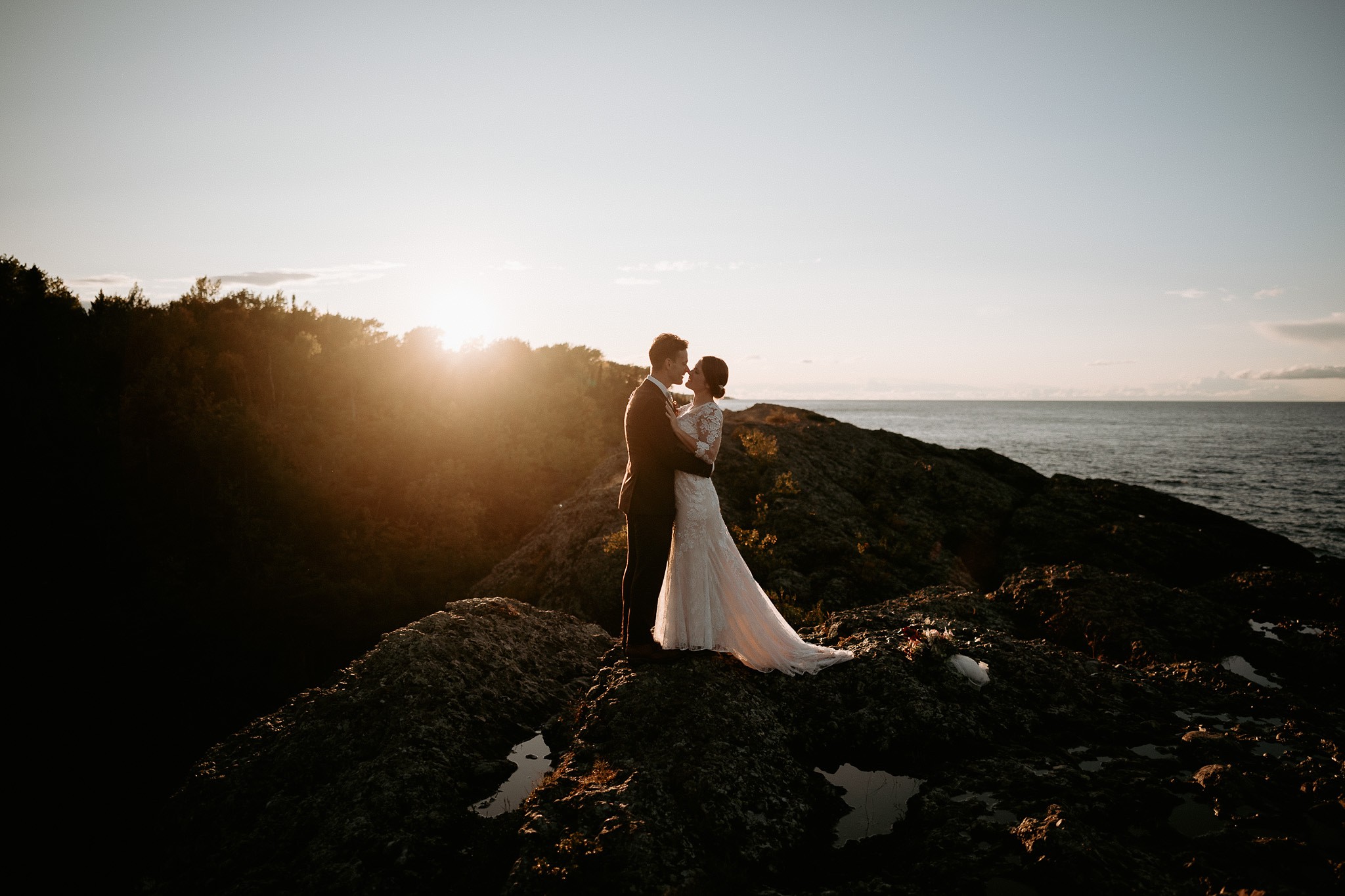 Bride and groom standing in sunlight on rocks in Copper Harbor, MI.